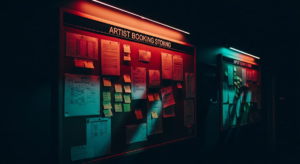 Illuminated booking board in a dim club corridor with dramatic pink and teal neon light, papers pinned to cork
