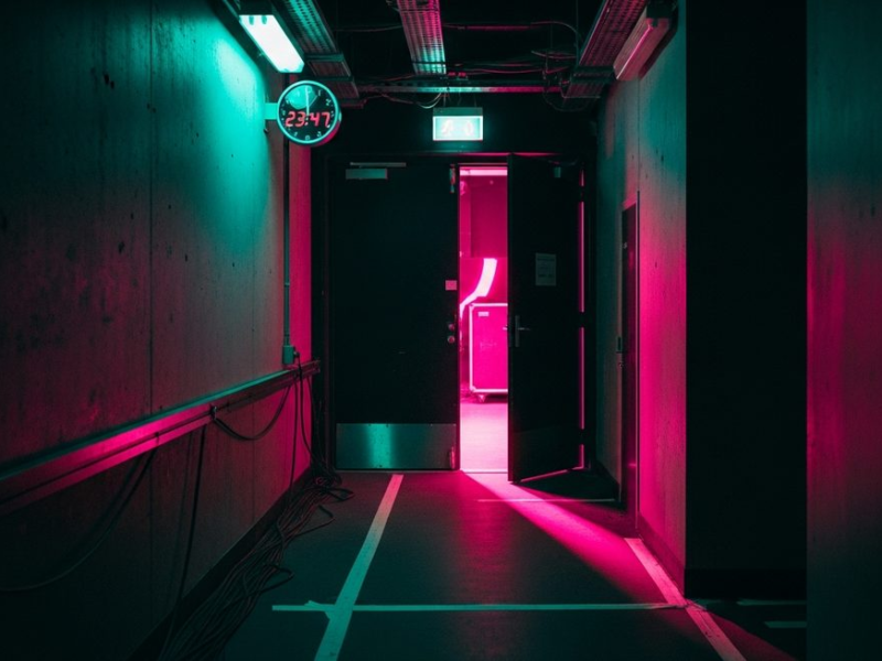 Narrow backstage corridor with clock and hot pink stage light bleeding through far door