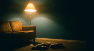 Low-lit late-night chill-out room, worn velvet sofa under amber floor lamp, vinyl albums on floor in foreground, deep teal shadow, smoke haze