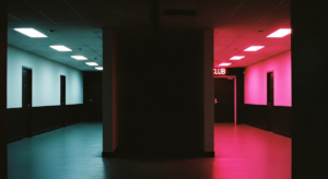 Long dark corridor with cold office fluorescent light at one end, hot pink club light at the other, complete shadow in the middle