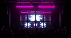 Looking into glowing DJ booth from dancefloor with hot pink neon and silhouetted crowd