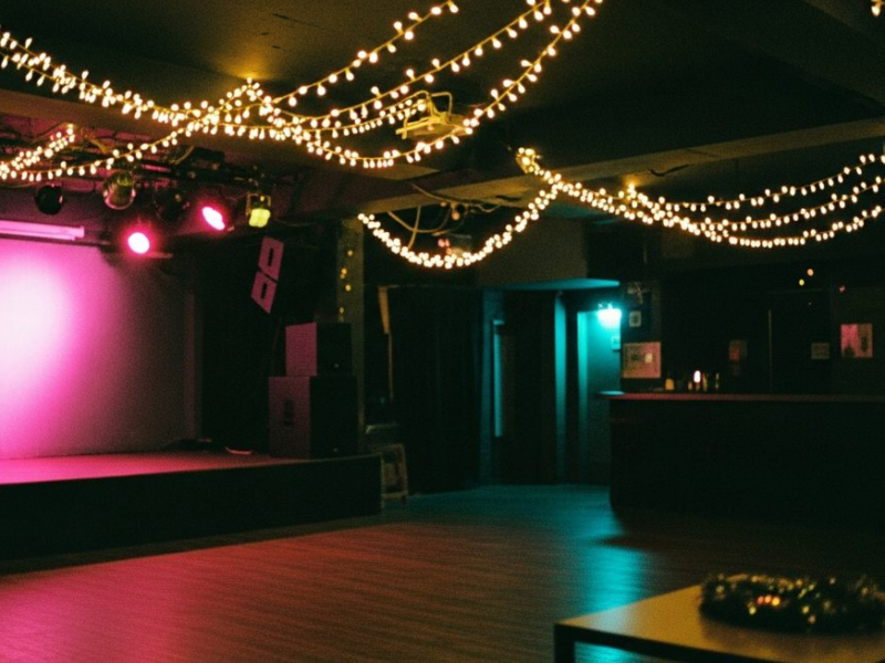 Intimate Seoul underground club on Christmas Eve, fairy lights and pink stage wash, empty dance floor, garland out of focus in foreground
