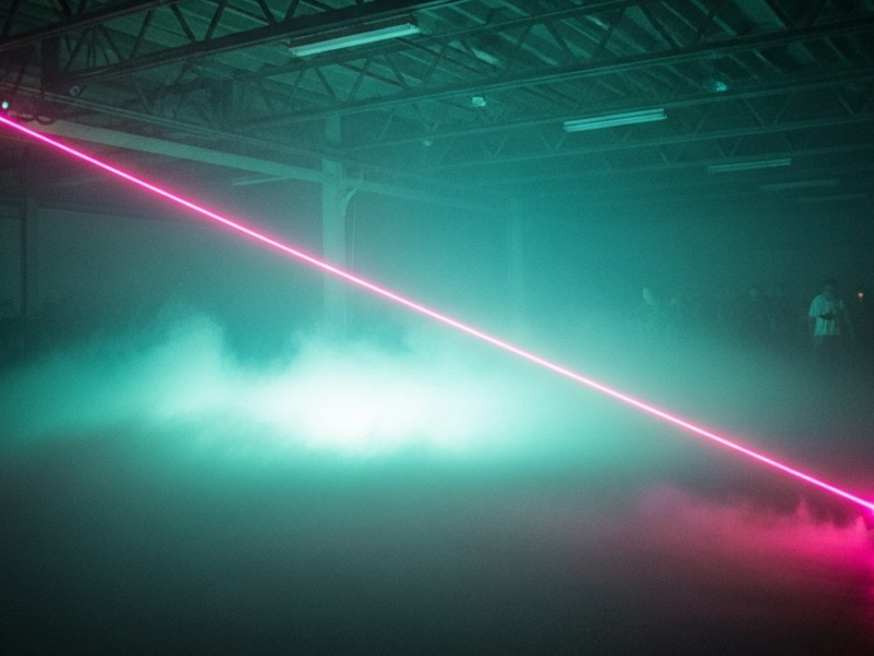Thick dry-ice fog rolling across a warehouse dance floor, pink laser cutting through the haze, teal light below, early 1990s rave atmosphere