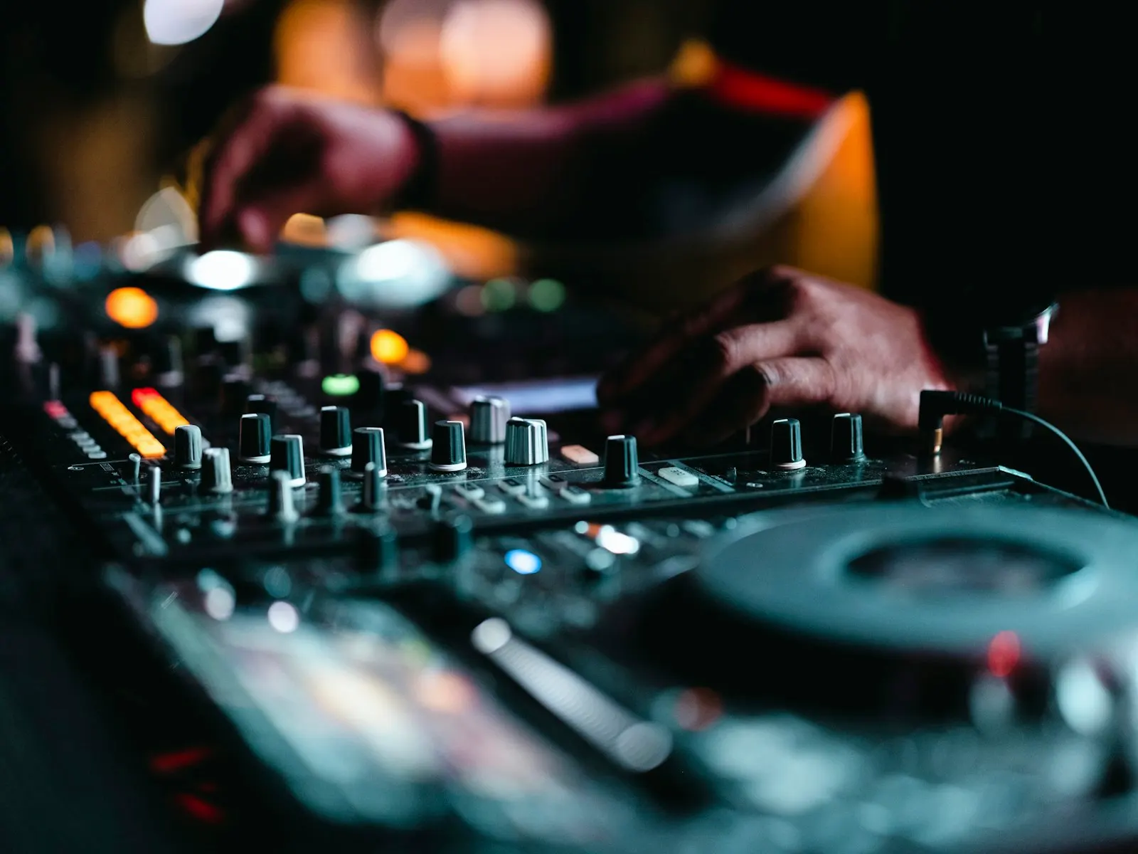 Close up of a DJ’s hands on a mixer under warm and blue booth light