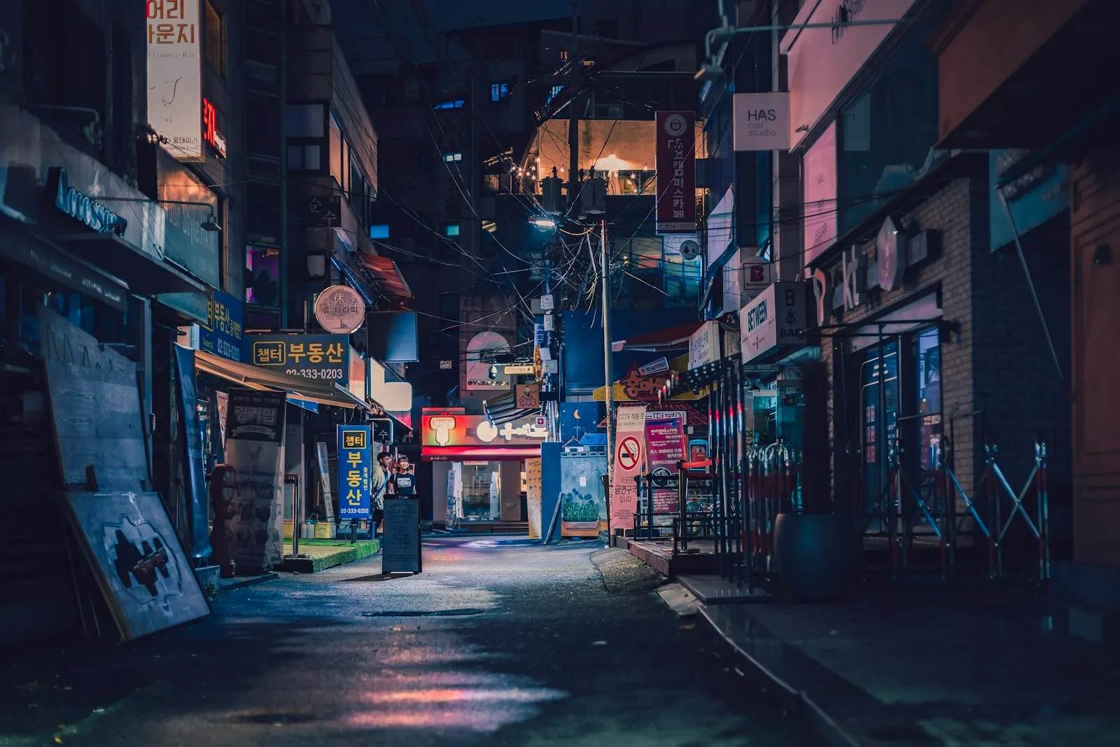 A quiet Hongdae side alley at night with neon spill on wet ground, Seoul