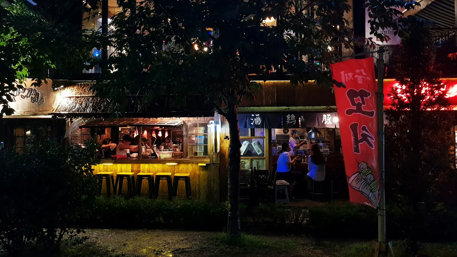 People at an outdoor bar under hangul banners on Hongdae street at night, Seoul