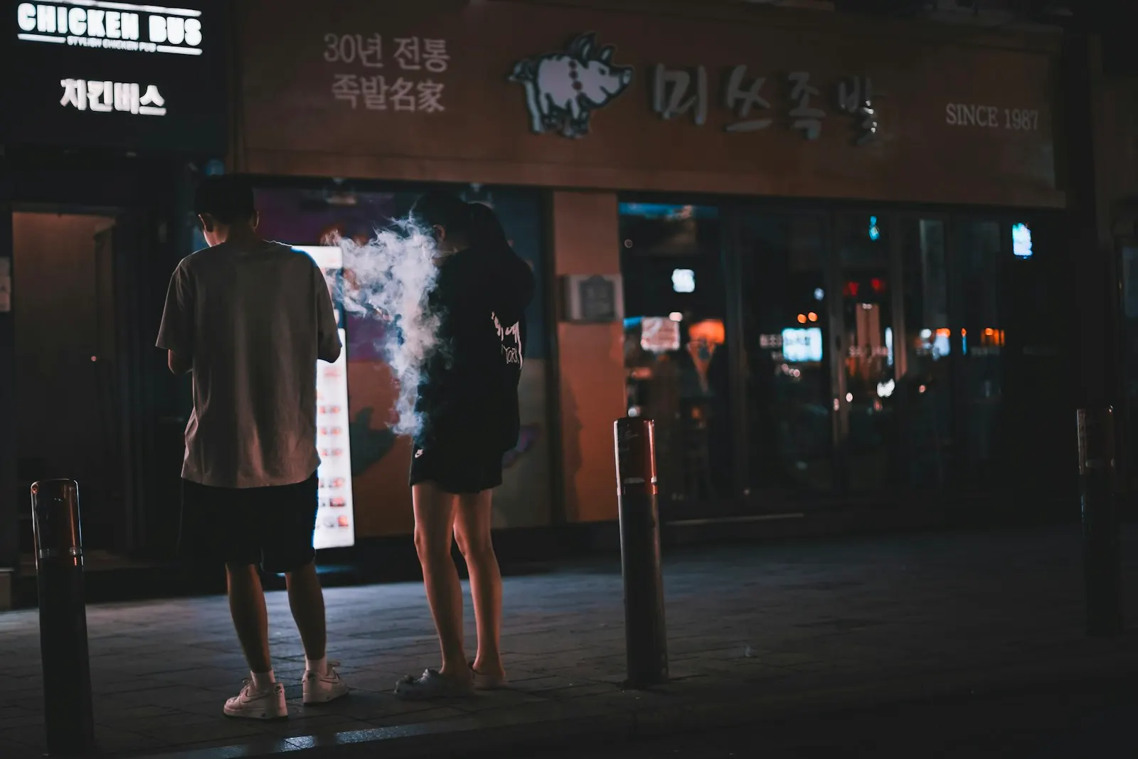 Two people with their backs to the camera outside a Hongdae bar at night, Seoul