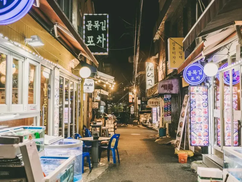 A narrow Itaewon-dong alley at night, lit tent bars and stacked crates, Seoul