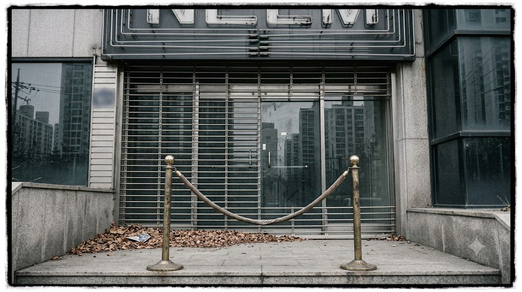 A closed-down Gangnam nightclub entrance in daylight: roller shutter down, dead neon sign, sagging velvet rope
