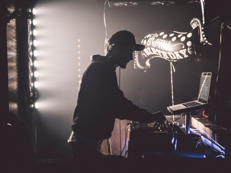 Silhouette of a DJ performing beside a 'Happy Birthday' balloon banner