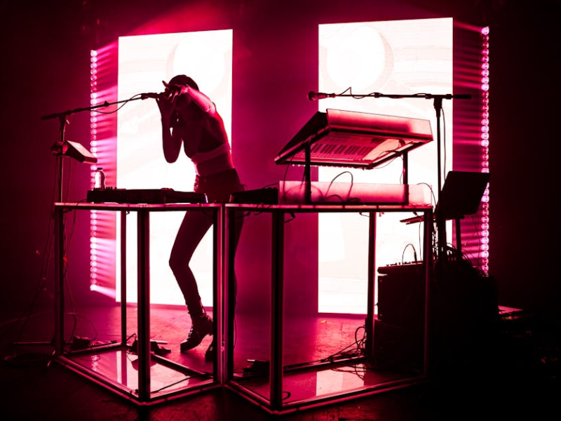 Silhouette of a performer singing into a microphone beside a keyboard under pink stage lights