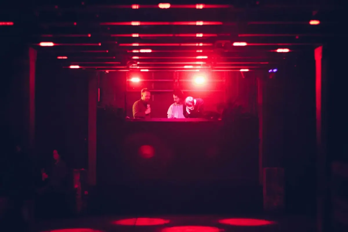 Two DJs lit red in a dark club booth