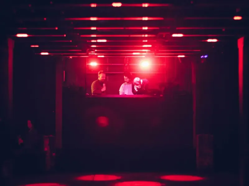 Two DJs lit red in a dark club booth