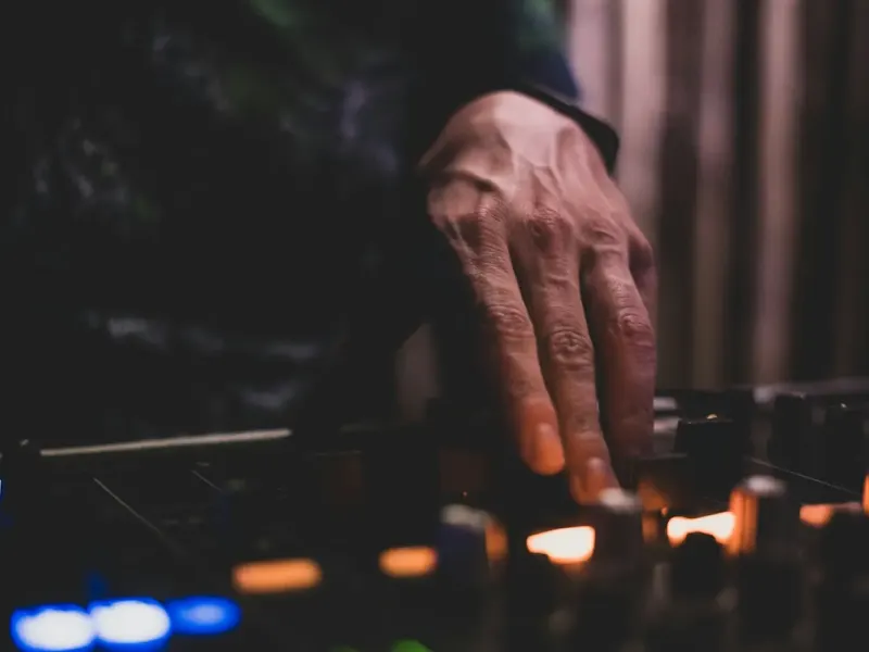 A DJ's hand on the mixer in a dark booth