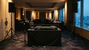 A compact DJ rig on a low stand in an empty hotel function room in Seoul, dinner tables set, city dusk in the windows
