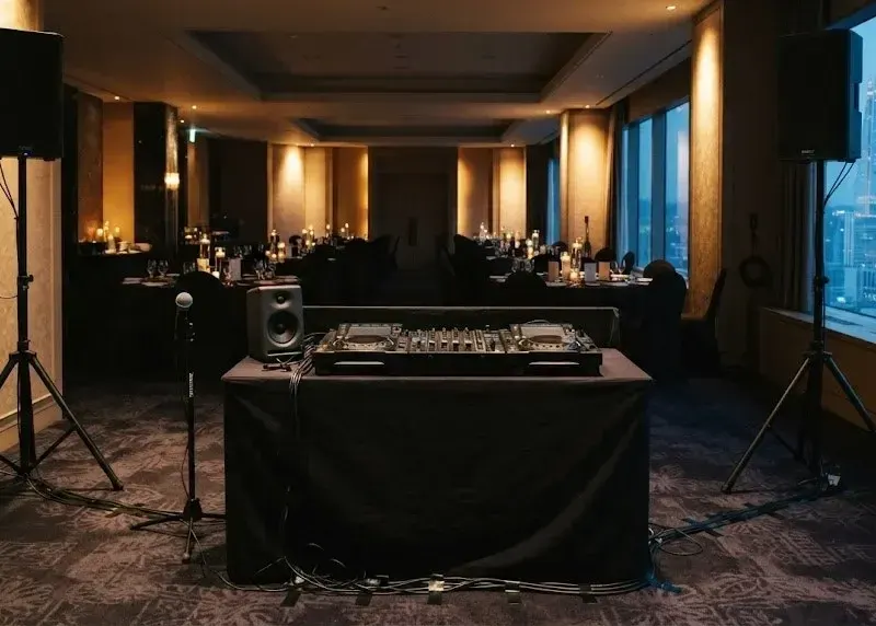 A compact DJ rig on a low stand in an empty hotel function room in Seoul, dinner tables set, city dusk in the windows