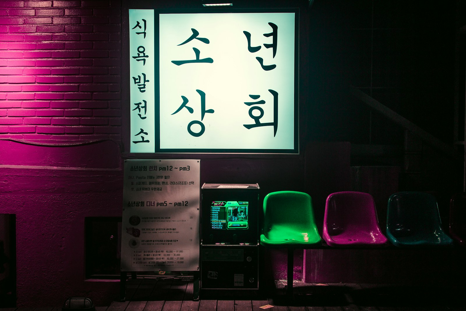 Small Seoul shop lit pink at night with empty stools