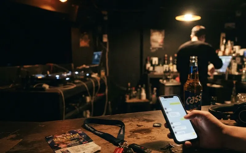Checking booking messages on a phone at the bar of a Seoul club before opening