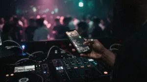 A DJ checks streaming numbers on a phone above the mixer in a dark booth