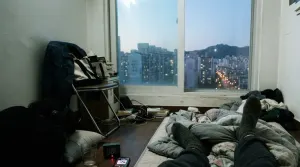 Lying on a floor mattress listening to music as dawn breaks over Seoul apartment blocks