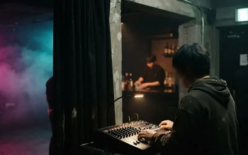 A sound engineer at the mixing desk while bar and door staff work behind him in a small Seoul club