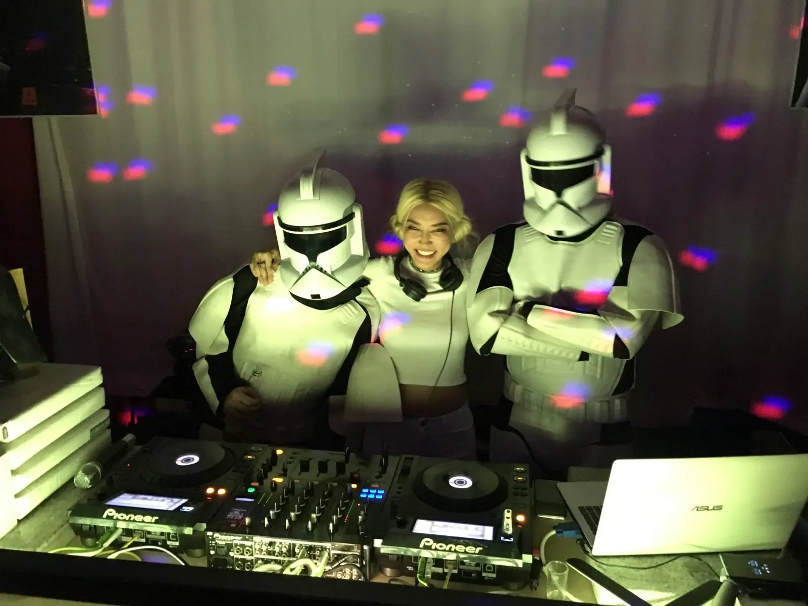 A smiling DJ in the booth between two people in clone trooper costumes