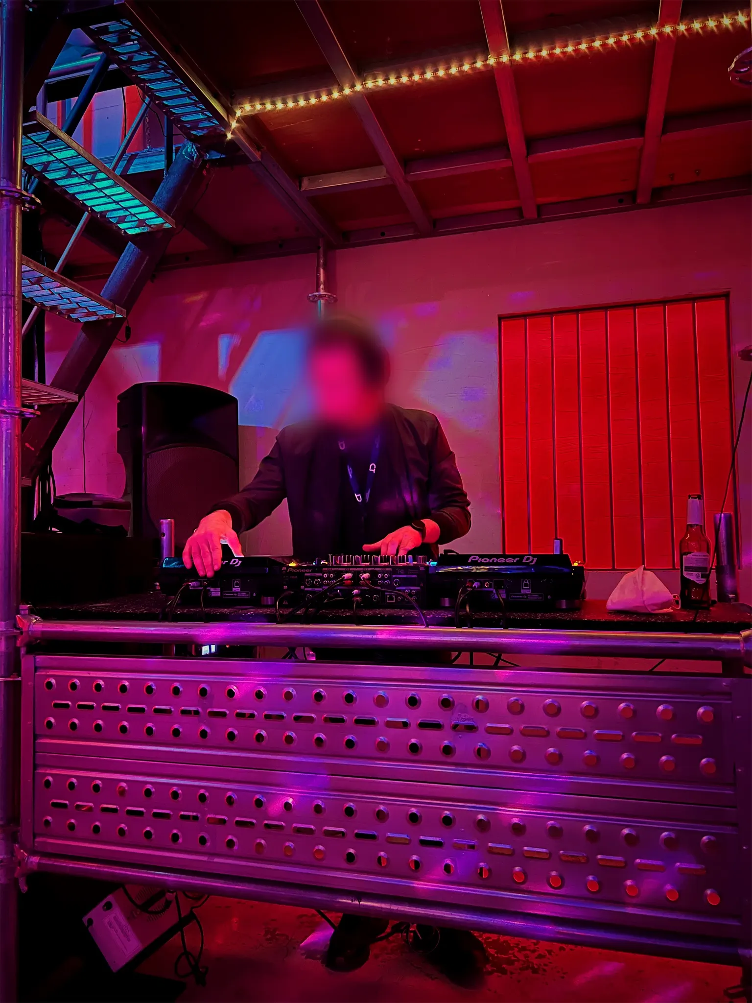 A DJ in headphones mixing on CDJs in a red and purple lit Hongdae booth.