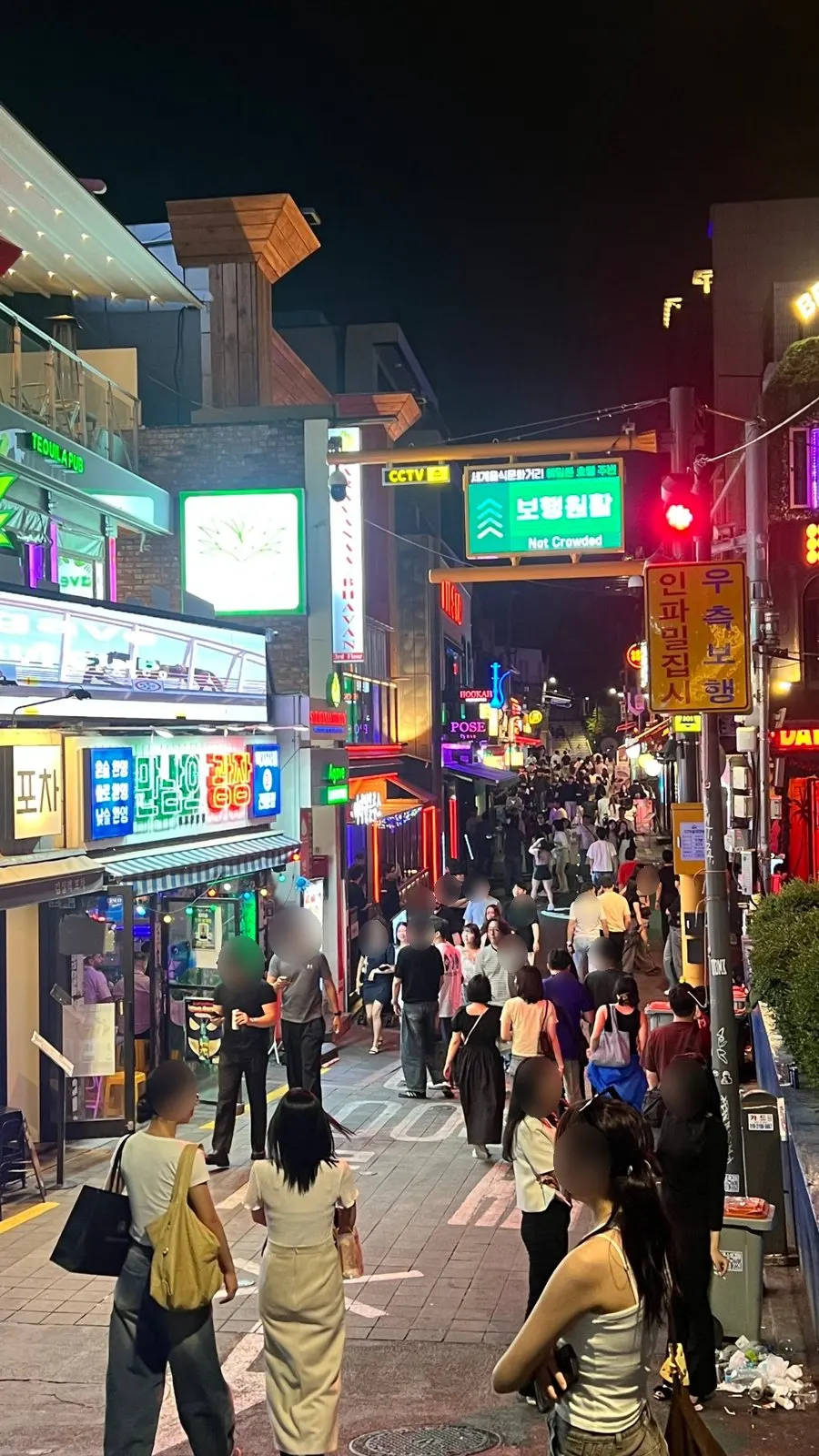 A congestion sign over World Food Street in Itaewon reading Not Crowded in green, beside a yellow sign telling people to keep right when it gets crowded