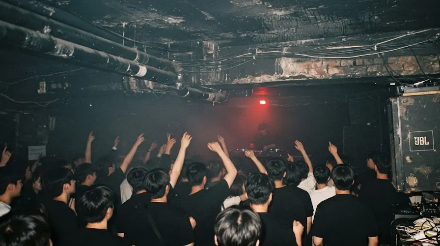 A packed basement dance floor in Seoul at 3am, hands up in the haze toward a silhouetted DJ
