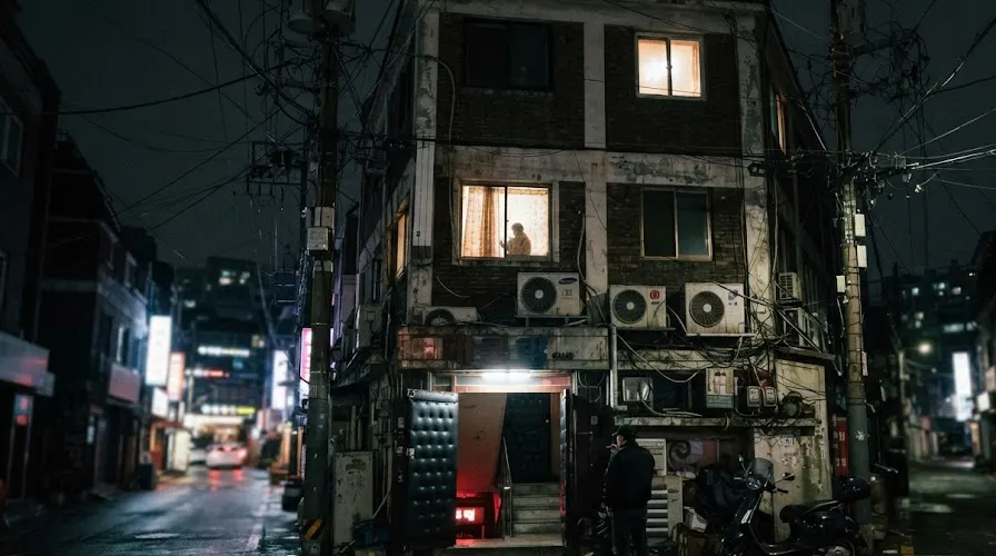 A basement club door at street level beneath small apartments on a Seoul side street at 2am